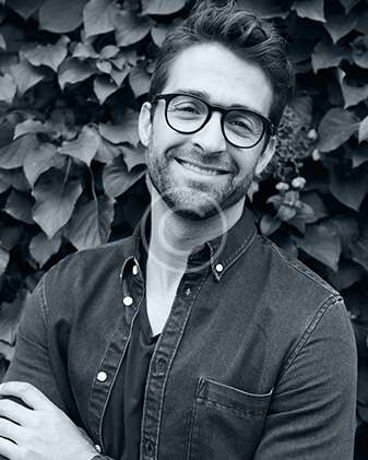 Smiling man with glasses in front of foliage, representing drone aerial photography services.